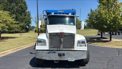 Kenworth T880S dump truck front view showing large grille, chrome bumper, rectangular headlights, blue dump bed canopy, and VIN/stock labels likely on cab.