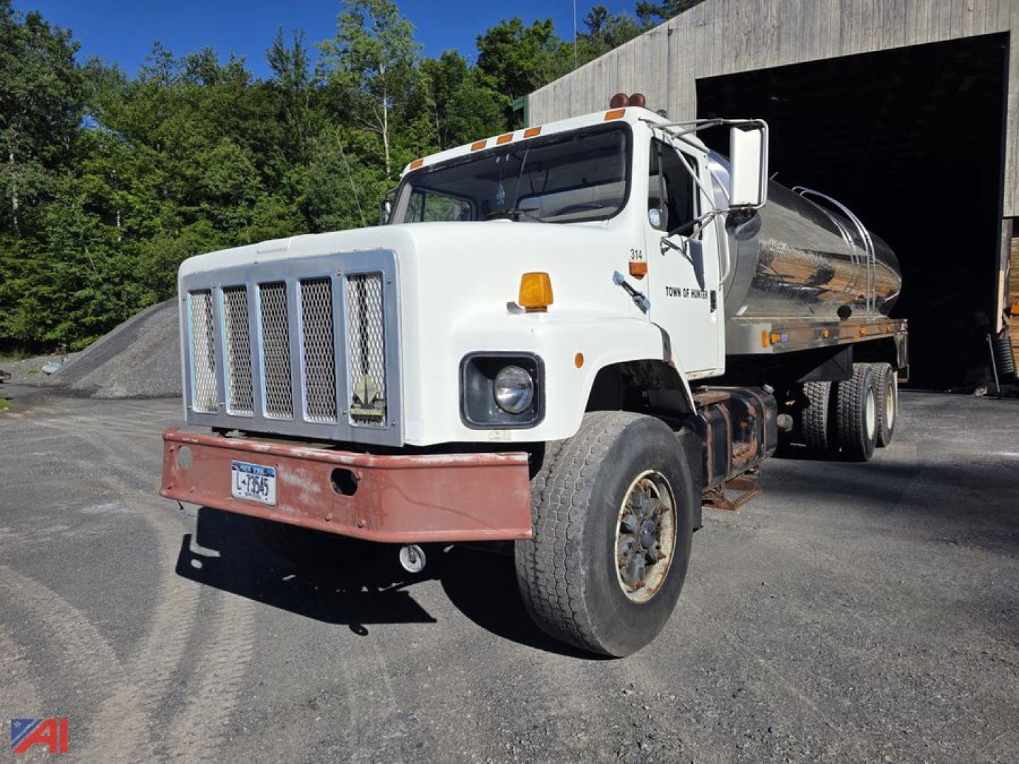 Water truck front-left view showing International 2674 tandem axle with stainless steel tank and chrome grille; front bumper guard; amber turn signals; side mirrors; large tires.