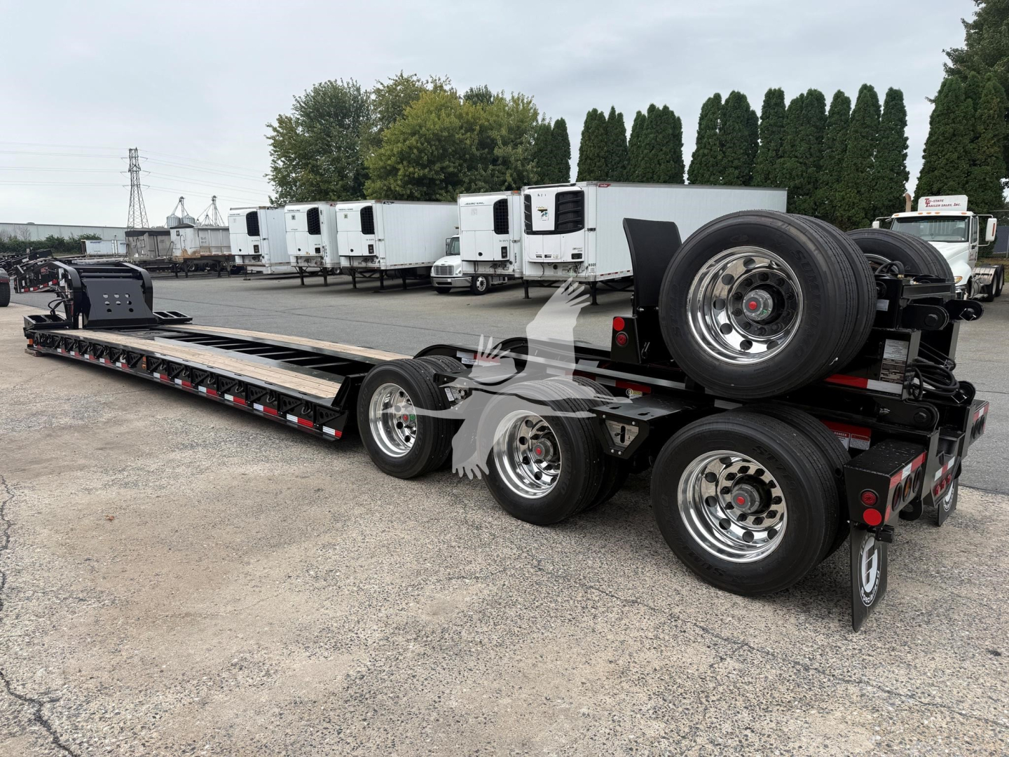 Fontaine Magnitude 60Lcc lowboy trailer showing long flat deck with multiple axles and a spare tire mounted on rear, in a dealership lot.