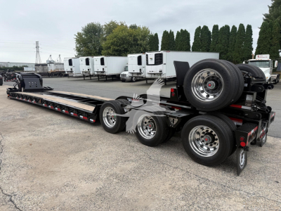  Fontaine Magnitude 60Lcc lowboy trailer showing long flat deck with multiple axles and a spare tire mounted on rear, in a dealership lot.