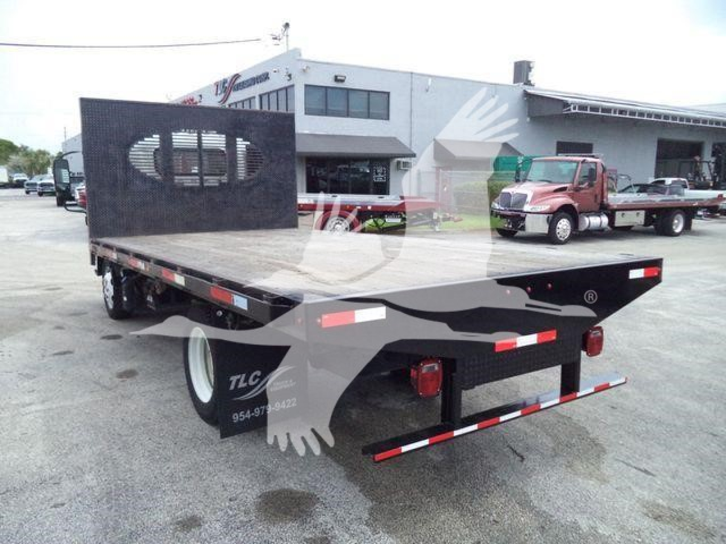 Isuzu NPRR flatbed truck trailer showing rear and left side with black metal headache rack and red tail lights.