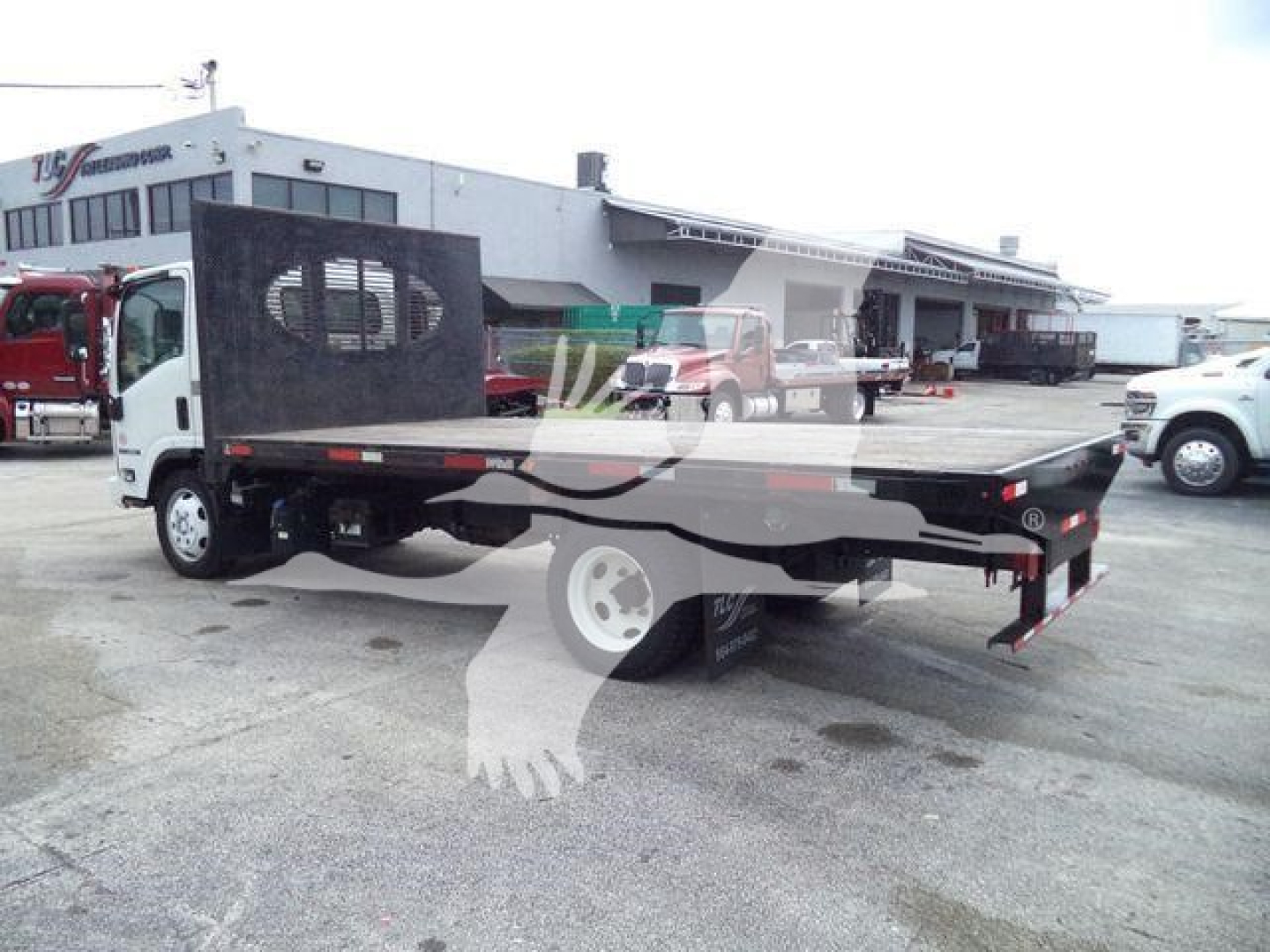 Isuzu NPR flatbed truck in a used inventory lot showing flatbed with steel deck and rear parking area.
