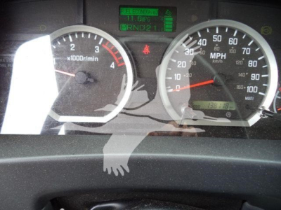 Dashboard view of a 2019 Isuzu NPRR flatbed truck showing two circular gauges (tachometer and speedometer) with a digital display in the center.