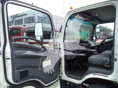 Isuzu NPRR cab interior with front left door open showing dashboard and steering wheel, view into the passenger cabin of a white flatbed truck.