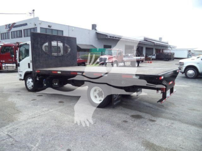 Isuzu NPR flatbed truck in a used inventory lot showing flatbed with steel deck and rear parking area.
