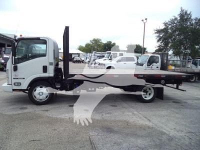 Isuzu NPR/flatbed tow truck side view showing truck cab and long flatbed with hydraulic ramp, white exterior, diesel engine, standard front axle and dual rear wheels.