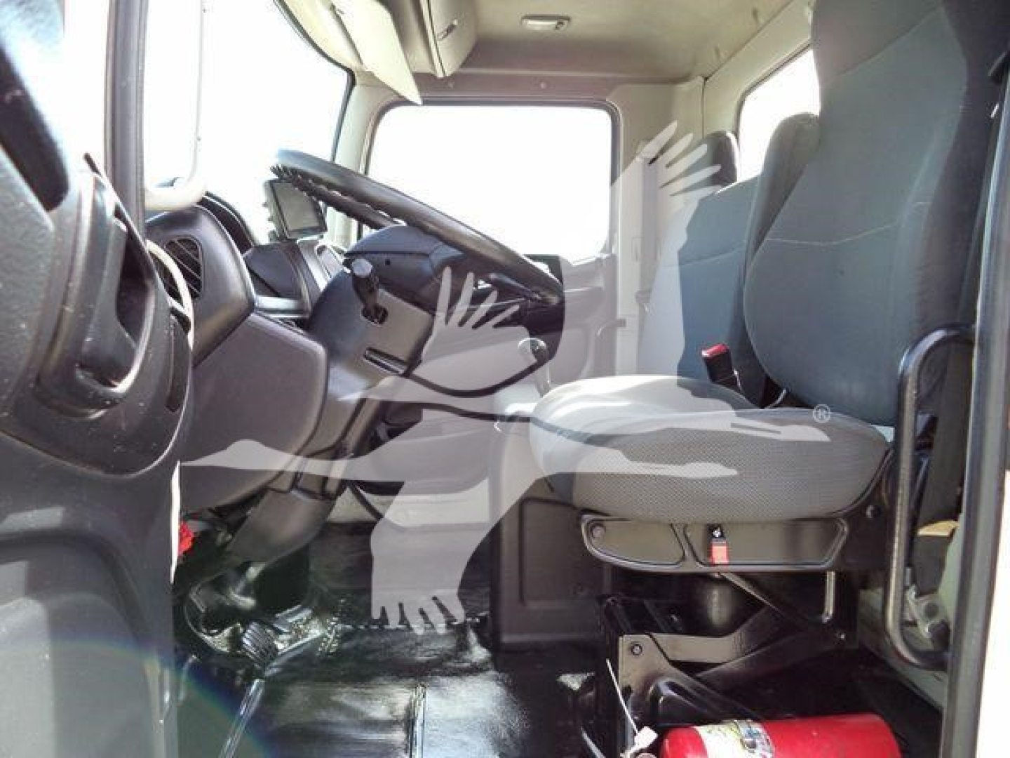 Truck cabin interior showing driver seat and steering wheel, with control panel and empty passenger seat; dash and floor mats visible.