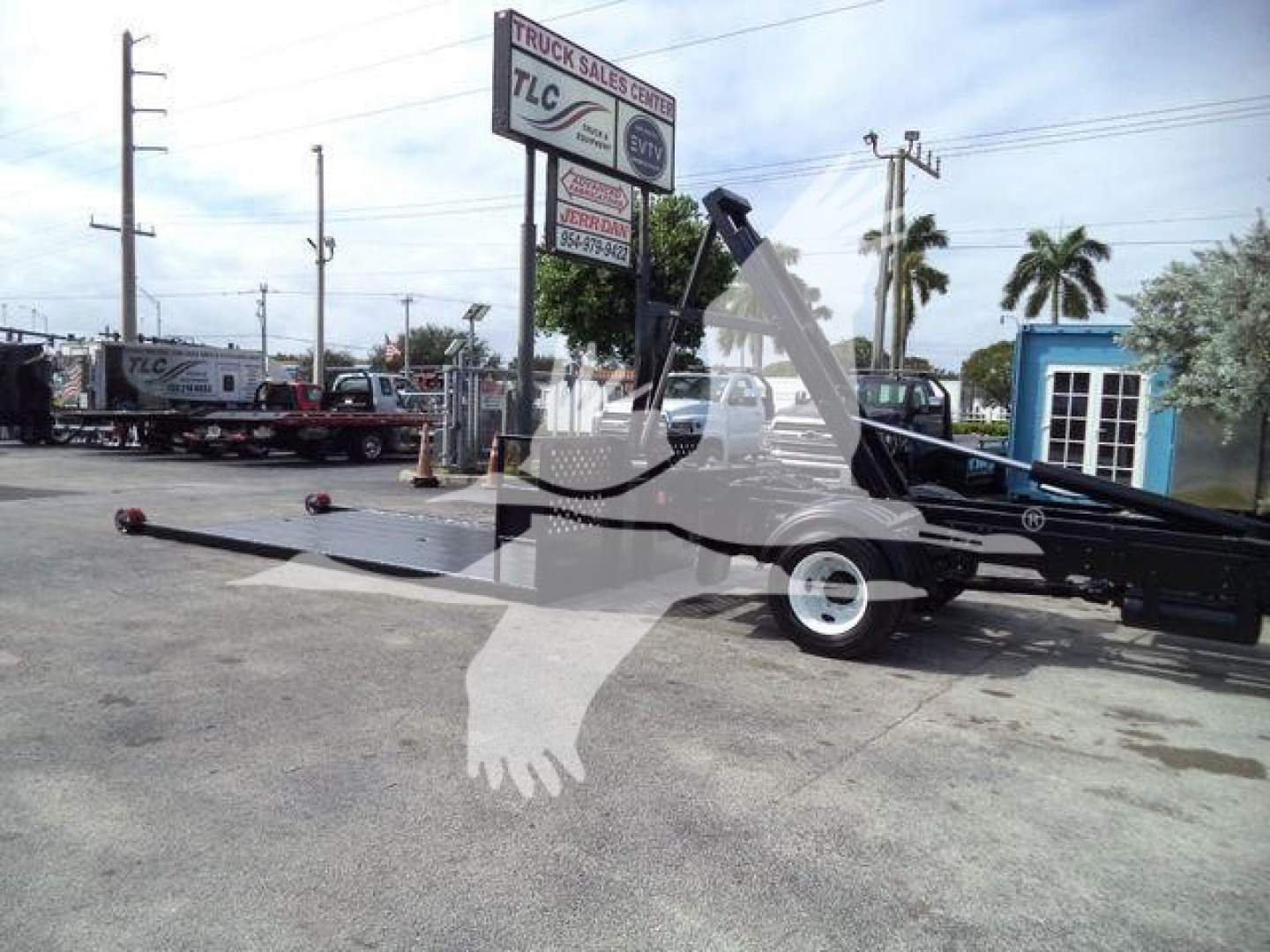 Hino 258LP hooklift truck with extended lift arm and trailer hitch, in a dealership lot with palm trees in background.