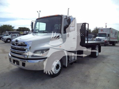 Hino 258LP hooklift truck front-left view showing cab and flatbed with wheel chocks and side controls.