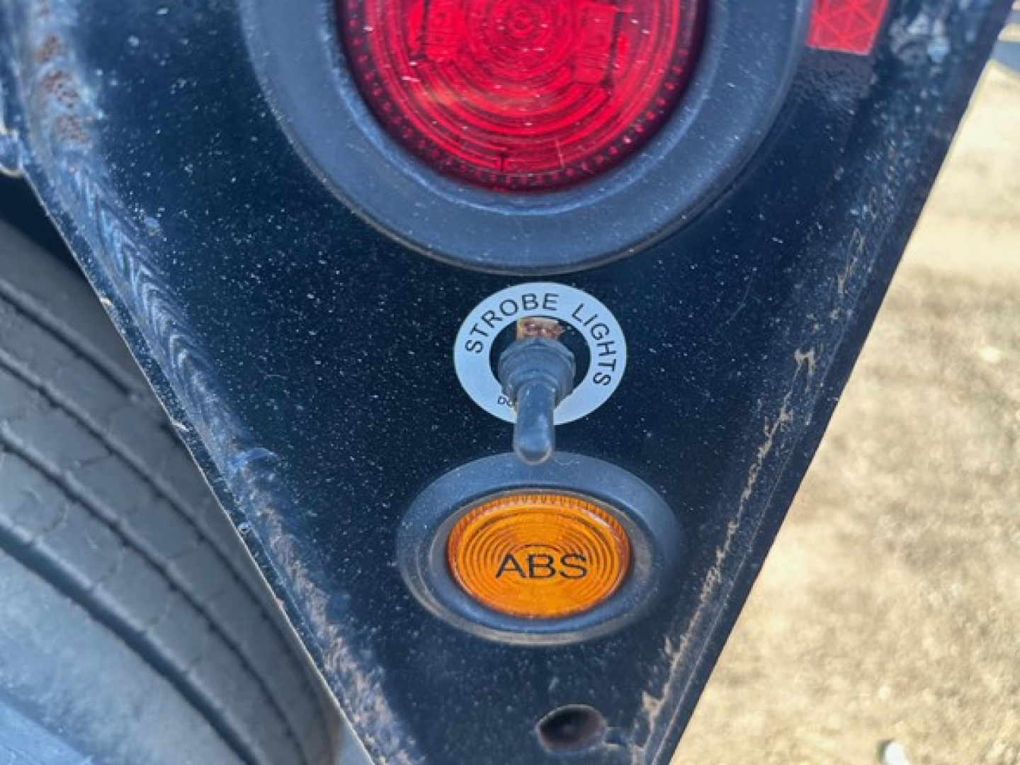 Trailer rear corner showing ABS indicator light and circular sticker reading STROBE LIGHTS with a toggle switch and red taillight above.