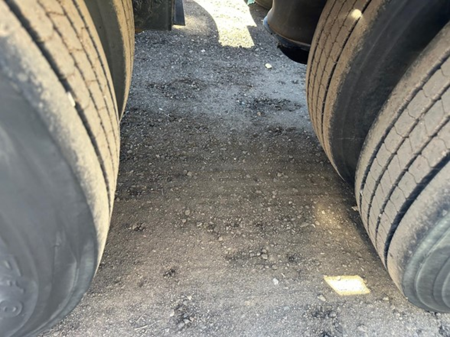 Trailer wheels and pavement between dual tires of a Kaufman lowboy trailer showing tread detail and gravel surface.