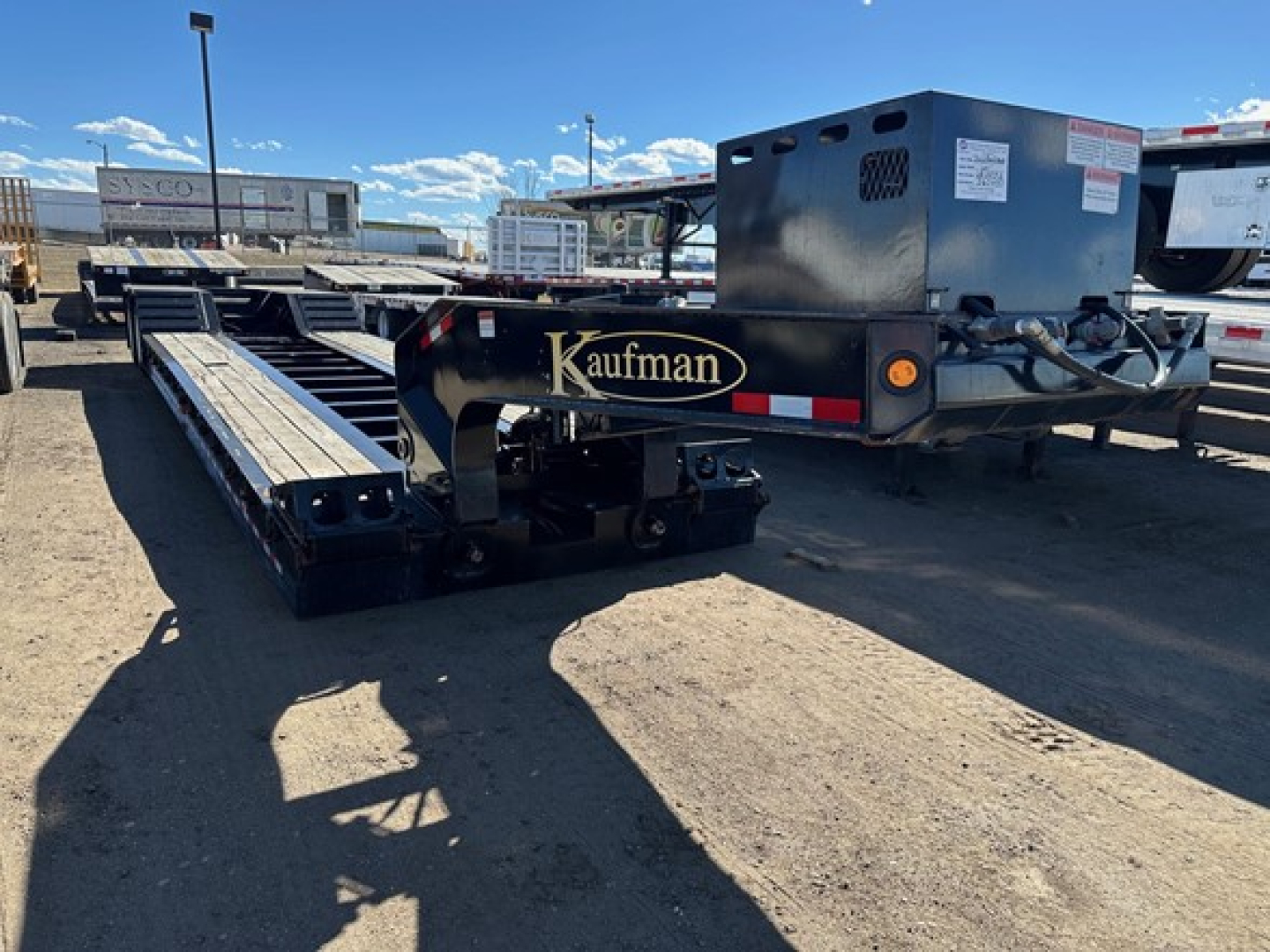 Kaufman lowboy trailer with pony motor, black and blue, long flatbed with dual rails and pony engine housing at rear.