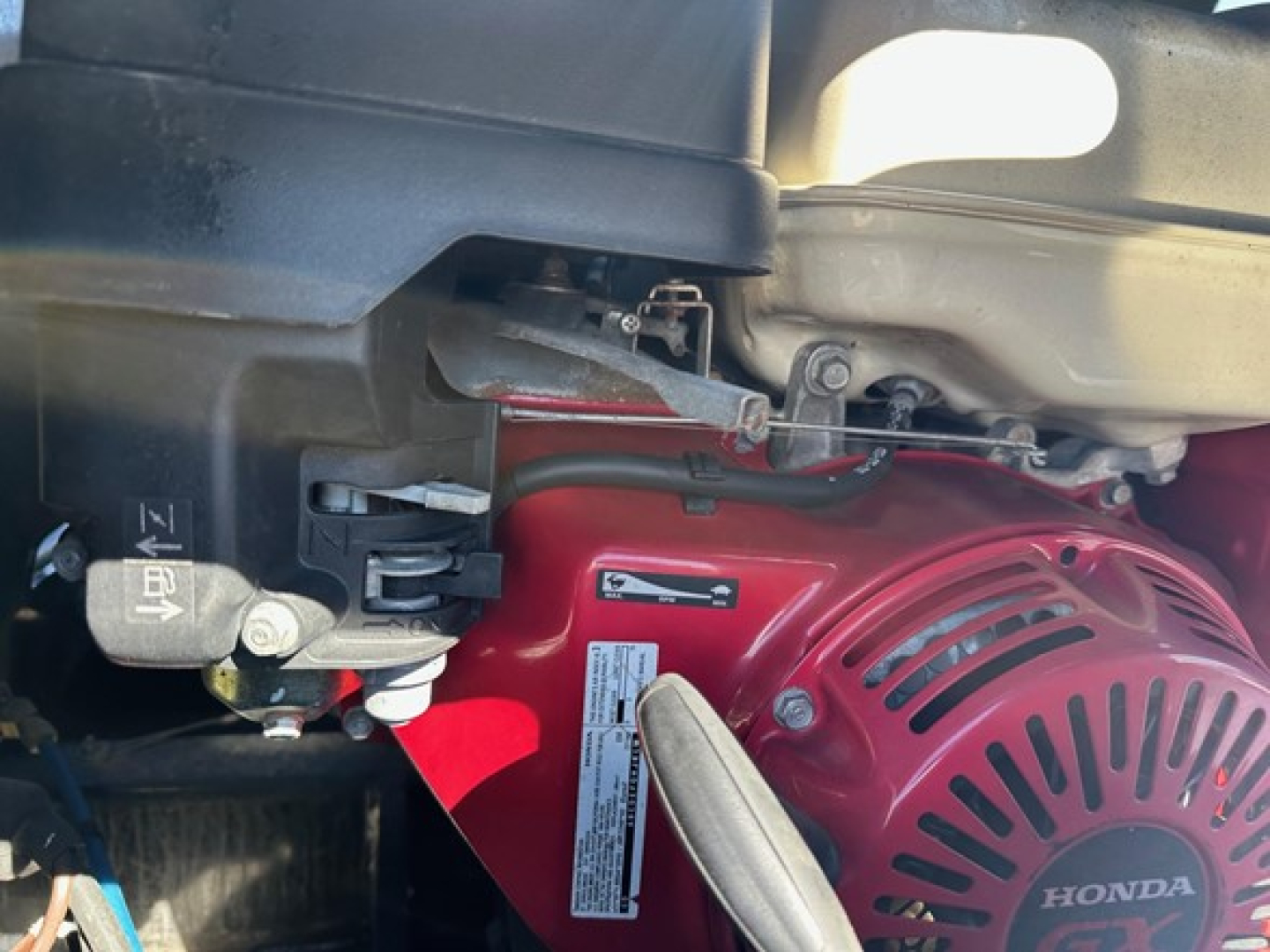 Lowboy trailer engine bay showing a red Honda pony motor with label, hoses, and wiring visible.