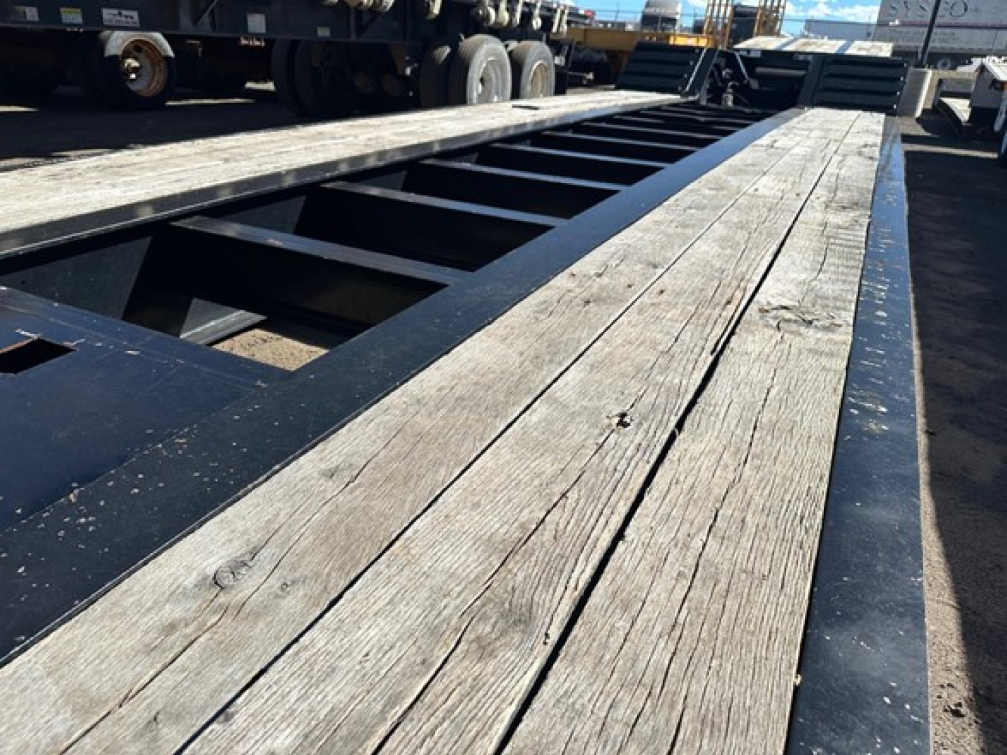 Lowboy trailer deck showing wooden planks and steel frame, Kuban/pony motor trailer components visible in distance.