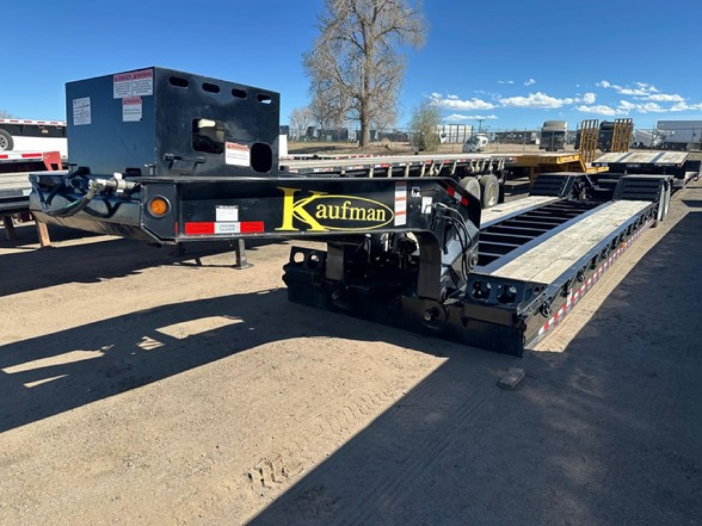 Kaufman lowboy trailer with pony motor and black frame showing yellow Kaufman branding on side, loading deck, and hitch area.