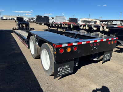 Lowboy trailer showing dual rear axles and flatbed deck with black side panels and round taillights.