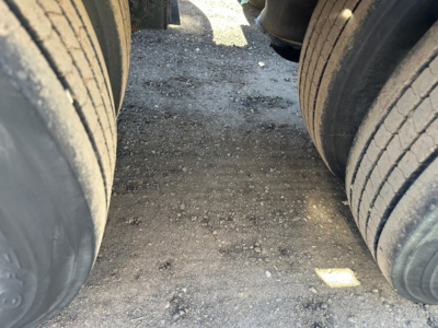 Trailer wheels and pavement between dual tires of a Kaufman lowboy trailer showing tread detail and gravel surface.