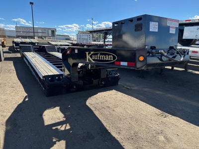 Kaufman lowboy trailer with pony motor, black and blue, long flatbed with dual rails and pony engine housing at rear.