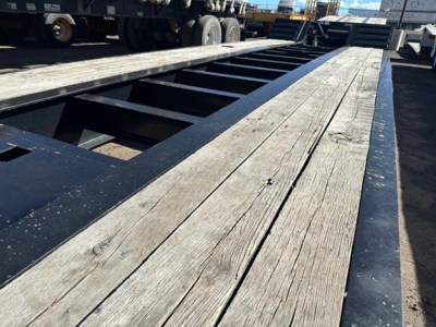 Lowboy trailer deck showing wooden planks and steel frame, Kuban/pony motor trailer components visible in distance.