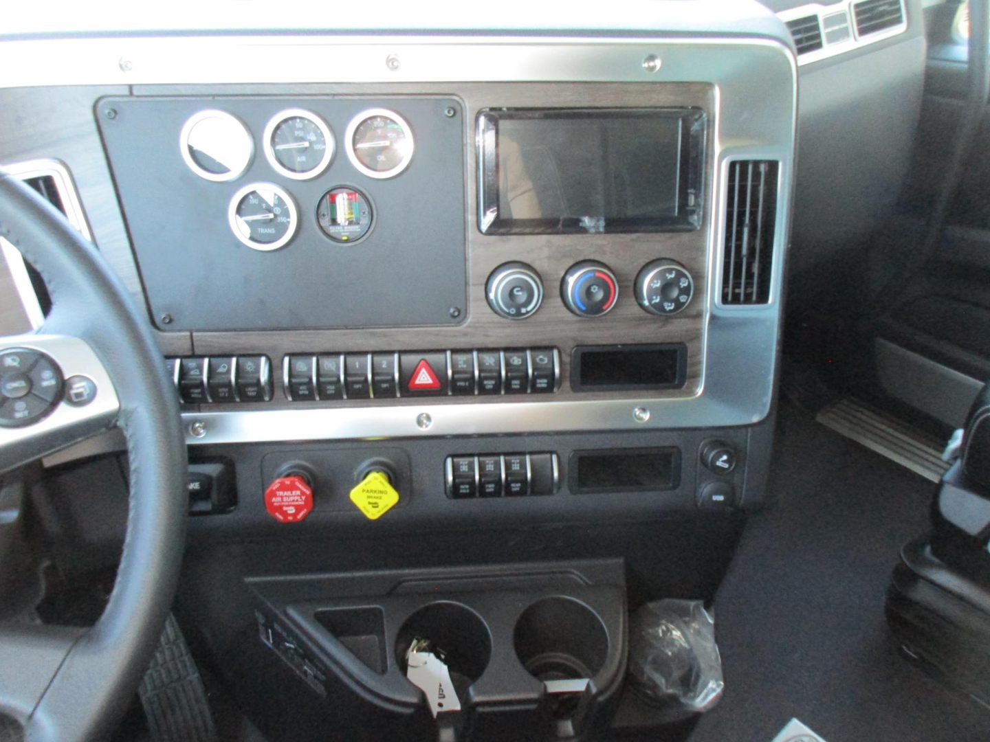 Dashboard of a Western Star 47X truck showing gauges, ignition area, control switches, touchscreen display, and cup holders.
