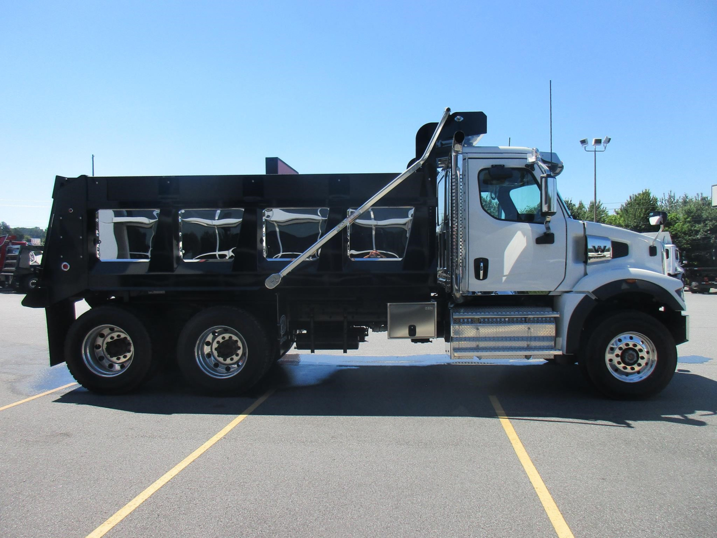 Dump truck side view showing large black dump bed, chrome exhaust stack, and front cab of a new Western Star 47X with six wheels in a parking lot.