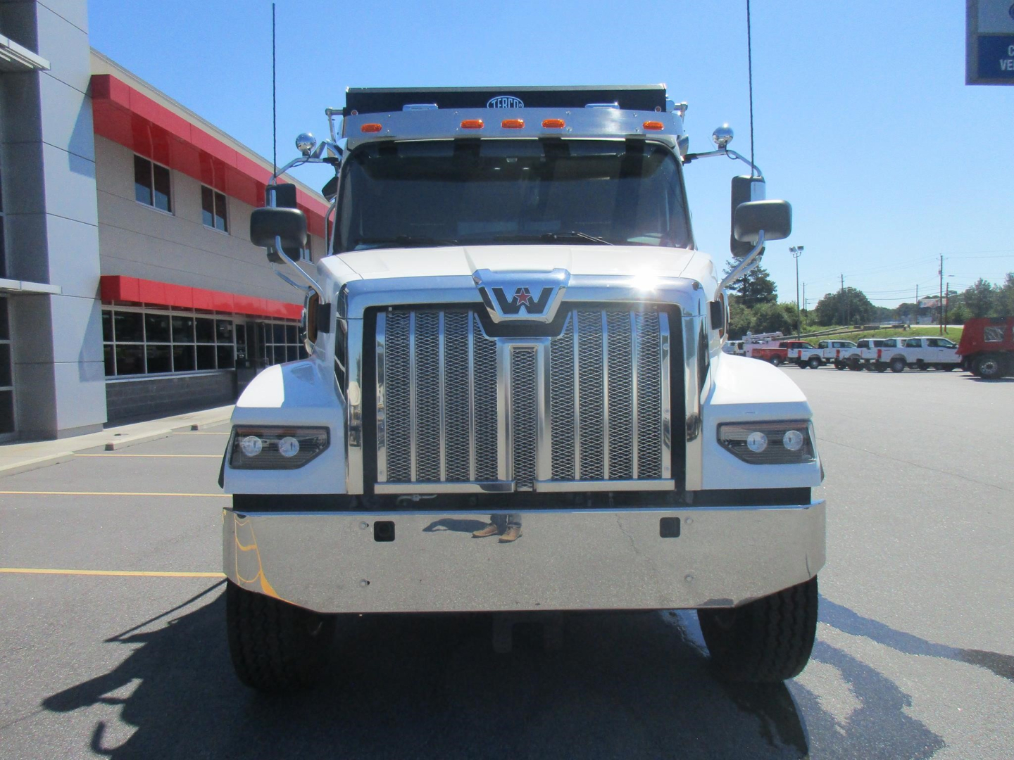 Front view of a 2027 Western Star 47X dump truck showing chrome grille, logo, headlights, and bumper; white cab with black mirrors in a dealership lot.
