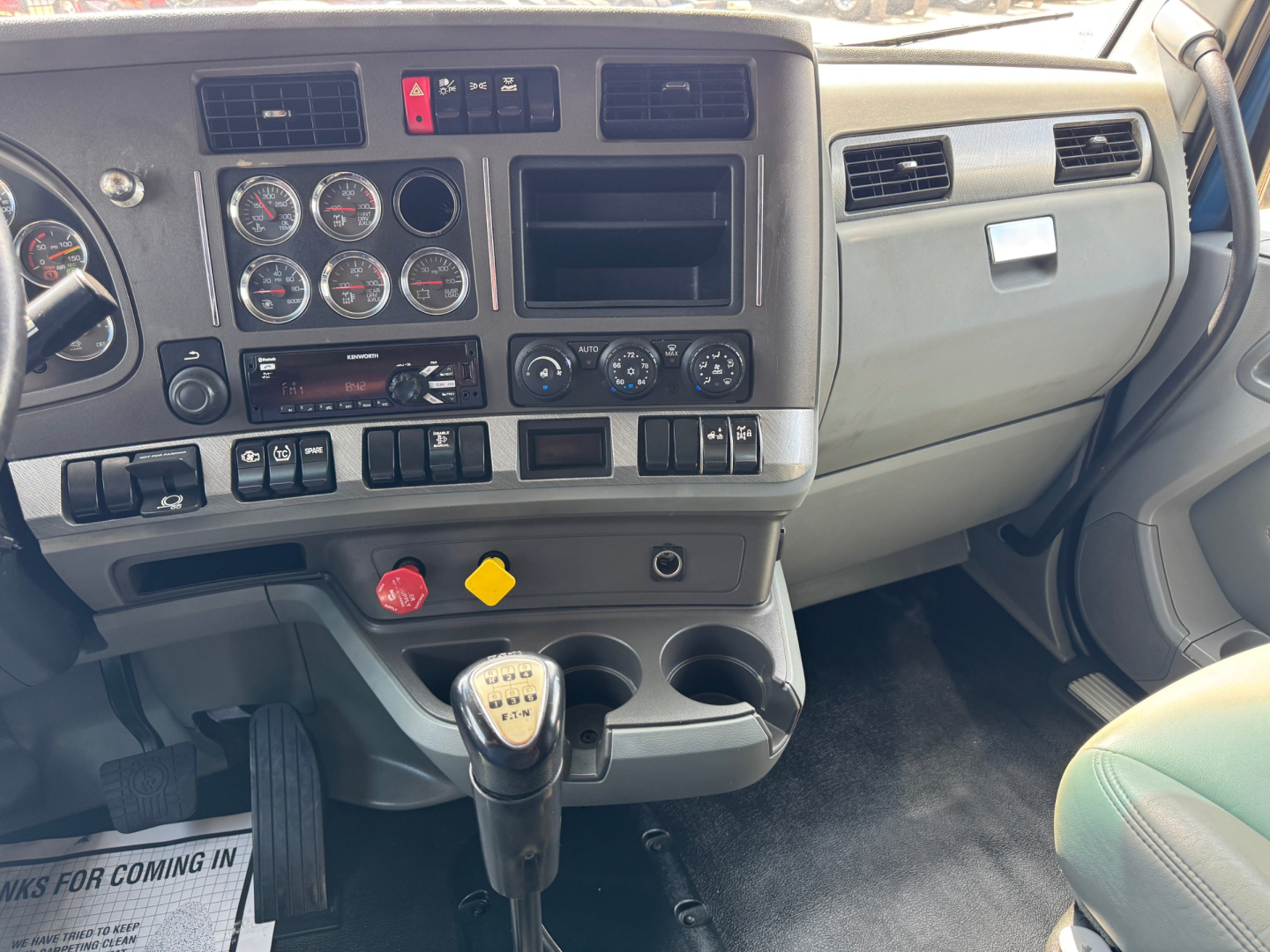 Kenworth T880 dash and center console showing controls, gauges, and manual gear shifter in cab interior.