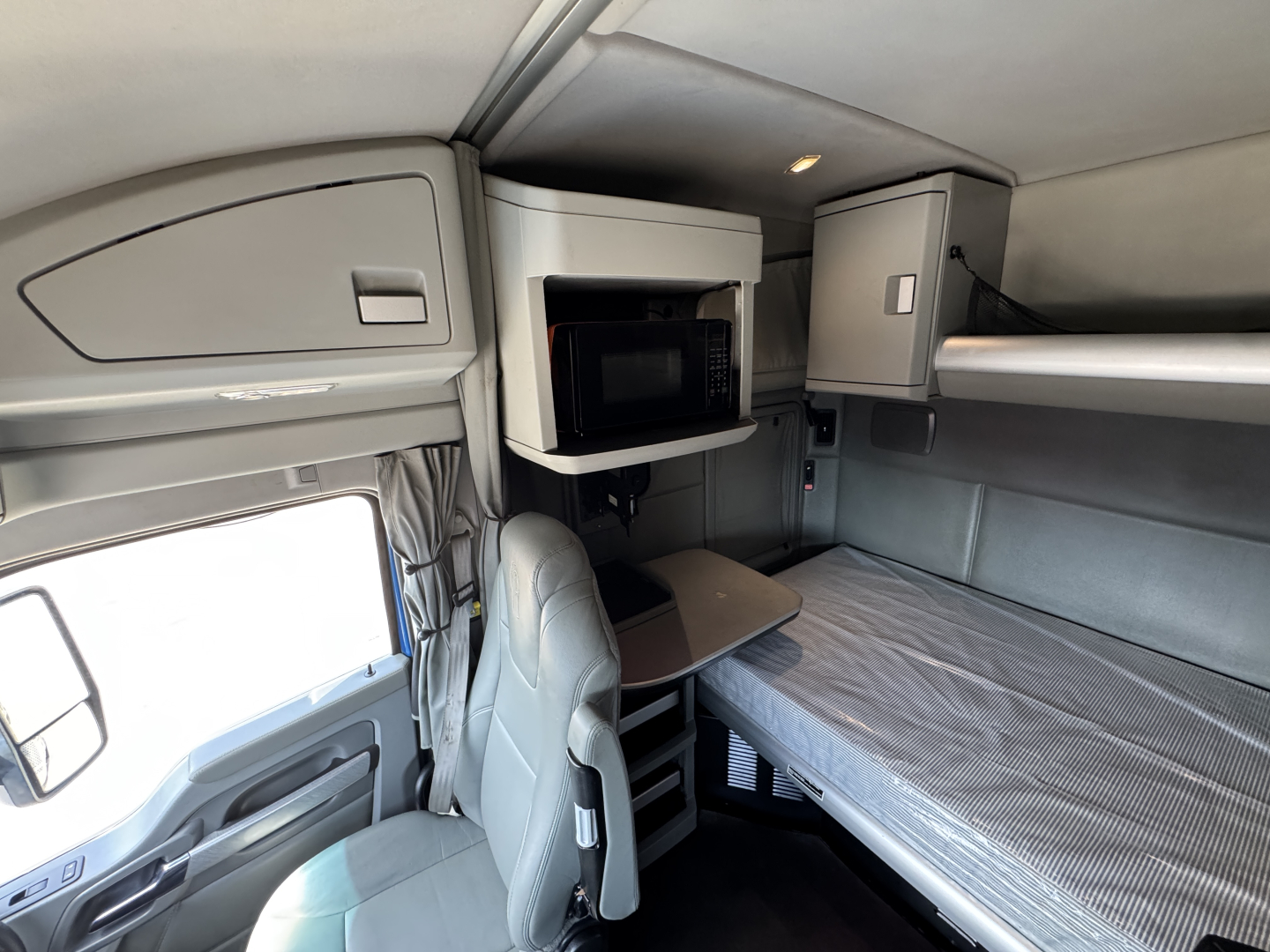 Kenworth T880 sleeper cab interior showing bunk, overhead storage, microwave, and seating area.