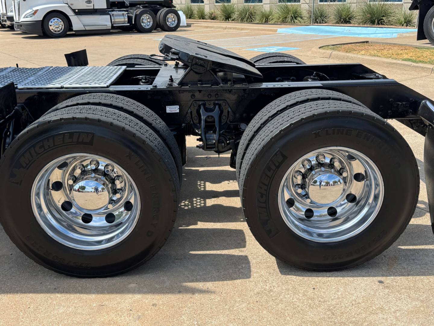 Dual rear axles and wheel assembly of a tractor trailer chassis showing chrome rims and Michelin tires under a Kenworth T880 undercarriage.