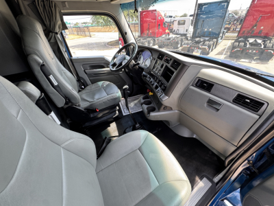 Kenworth T880 interior cab view showing steering wheel, dash, and driver seat. Light gray vinyl seats and beige dashboard with center console and gear shifter.