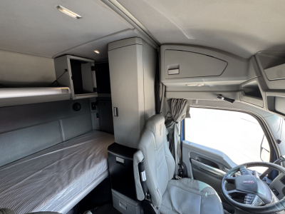 Cabin view of 2019 Kenworth T880 showing sleeper bunk and driver seat with overhead storage and dashboard window.