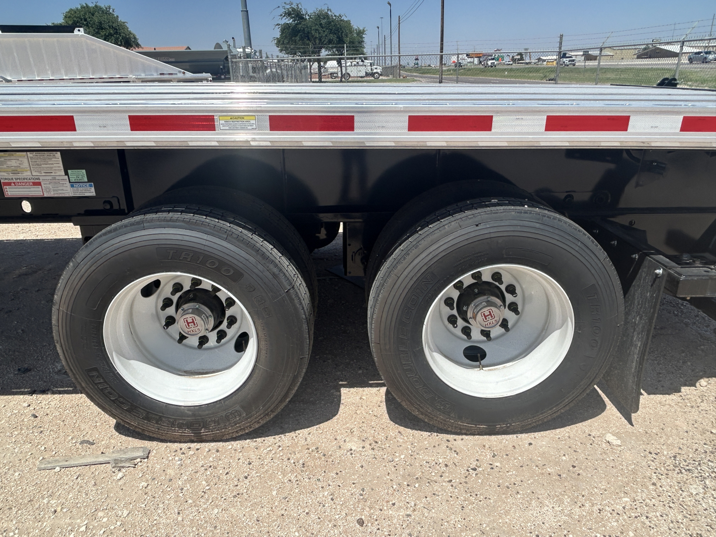 Flatbed trailer dual rear wheels showing tires and white rims on a Fontaine HCIFL12SAT trailer.