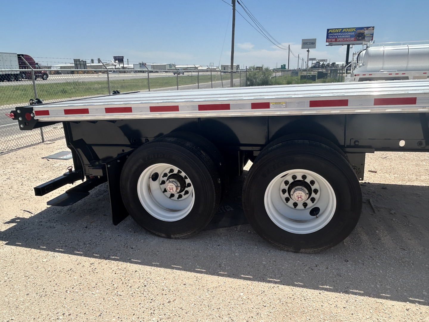 Flatbed trailer wheel area showing tandem axles and white rims, Fontaine HCIFL12SAT trailer model badge not visible.