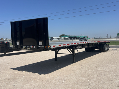 Flatbed trailer showing black hydraulic gooseneck and long flat deck with tandem axles and landing gear.