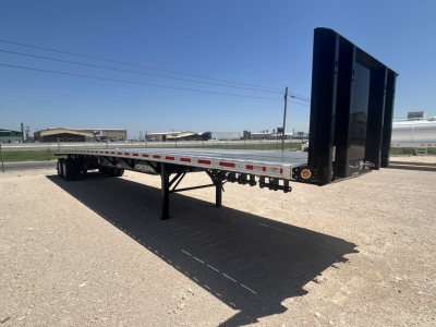 Flatbed trailer with black drop-down tail and gooseneck visible, side rails, and support legs; no legible text visible on the trailer side in this view.