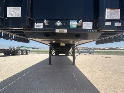 Trailer underside showing rear coupling and hydraulic components with inspection labels and stickers.