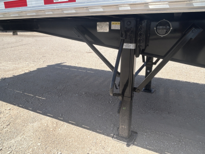 Flatbed trailer undercarriage showing landing gear with stabilizer legs and support braces.