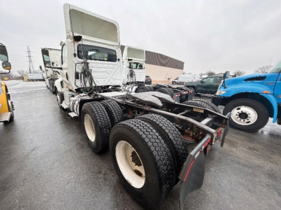 Tractor truck chassis and cab in a used truck lot showing LT625 6x4 rear view with dual rear axles and fifth wheel; white wheels, exposed drivetrain, other trucks in background.