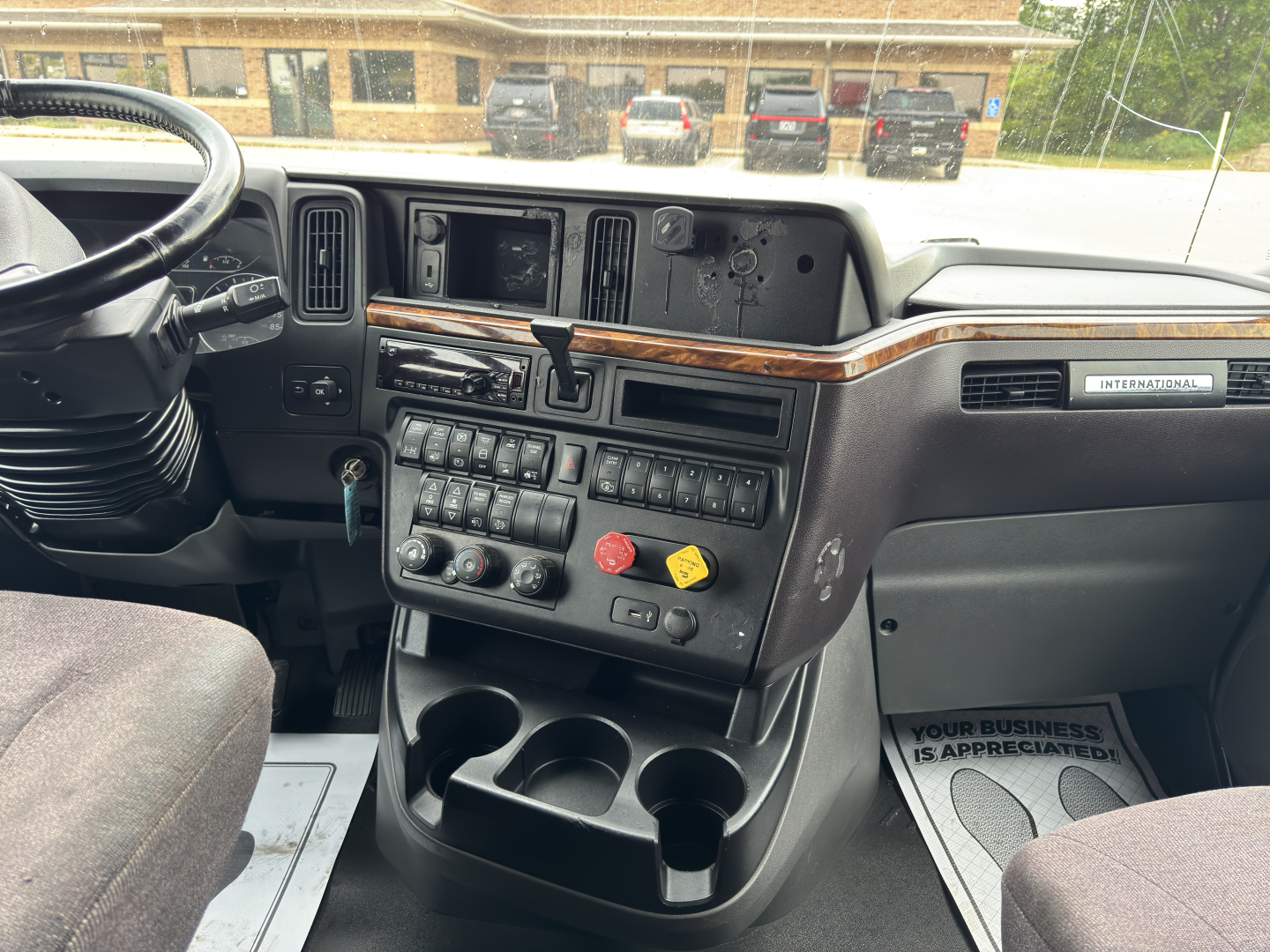 Truck cab interior showing dashboard with numerous switches, cup holders, and wood trim; International branding badge visible.
