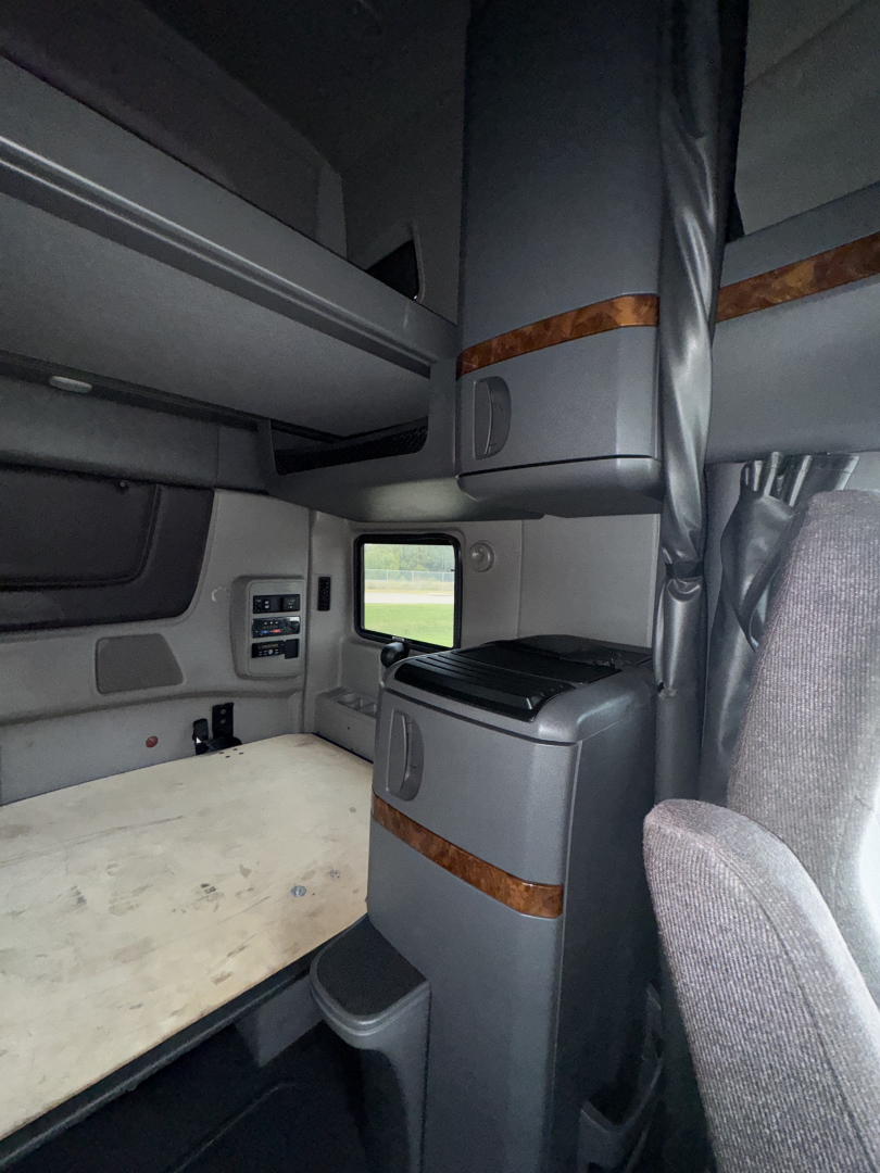 Interior sleeper cab of a 2018 International LT625 showing bunk area, side cabinet with wood trim, and upper storage shelf.