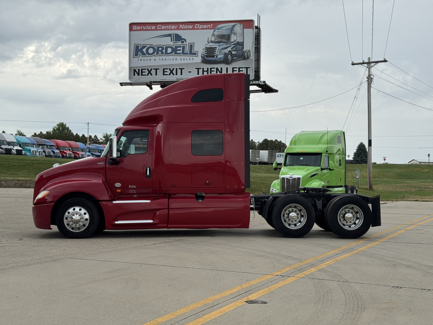 2018 International LT625 sleeper tractor with red cab and green trailer unit, side view, on road with billboard in background.