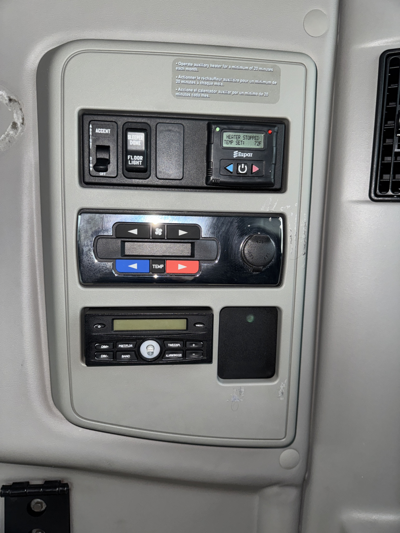 Dashboard panel in truck cab showing control switches and digital readout. Labels read: 'FLOOR' 'AIR' and various arrows; temperature/air controls; radio/CD slot area; blank screens.
