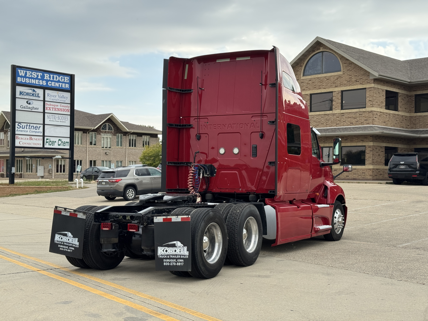 Truck cab rear and side view showing International LT625 sleeper tractor in red with dual rear axles and mud flaps; dealership lot in background.