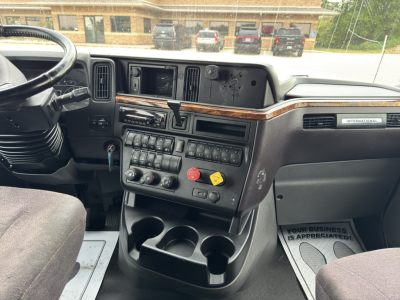 Truck cab interior showing dashboard with numerous switches, cup holders, and wood trim; International branding badge visible.