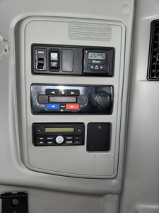 Dashboard panel in truck cab showing control switches and digital readout. Labels read: 'FLOOR' 'AIR' and various arrows; temperature/air controls; radio/CD slot area; blank screens.