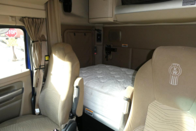 Kenworth T680 sleeper cab interior with bunk bed, front seats, beige upholstery, and dashboard area visible.
