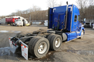Kenworth T680 tractor-trailer cab in blue, side view showing hybrid sleeper, rear axle configuration with dual rear axles and fifth wheel, top exhaust stack visible.