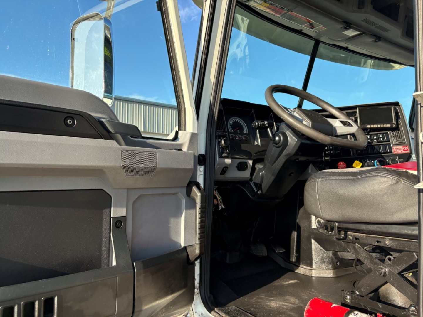 Truck cab interior of a 2023 Mack GR84F dump truck showing steering wheel, dashboard, and driver seat with open door