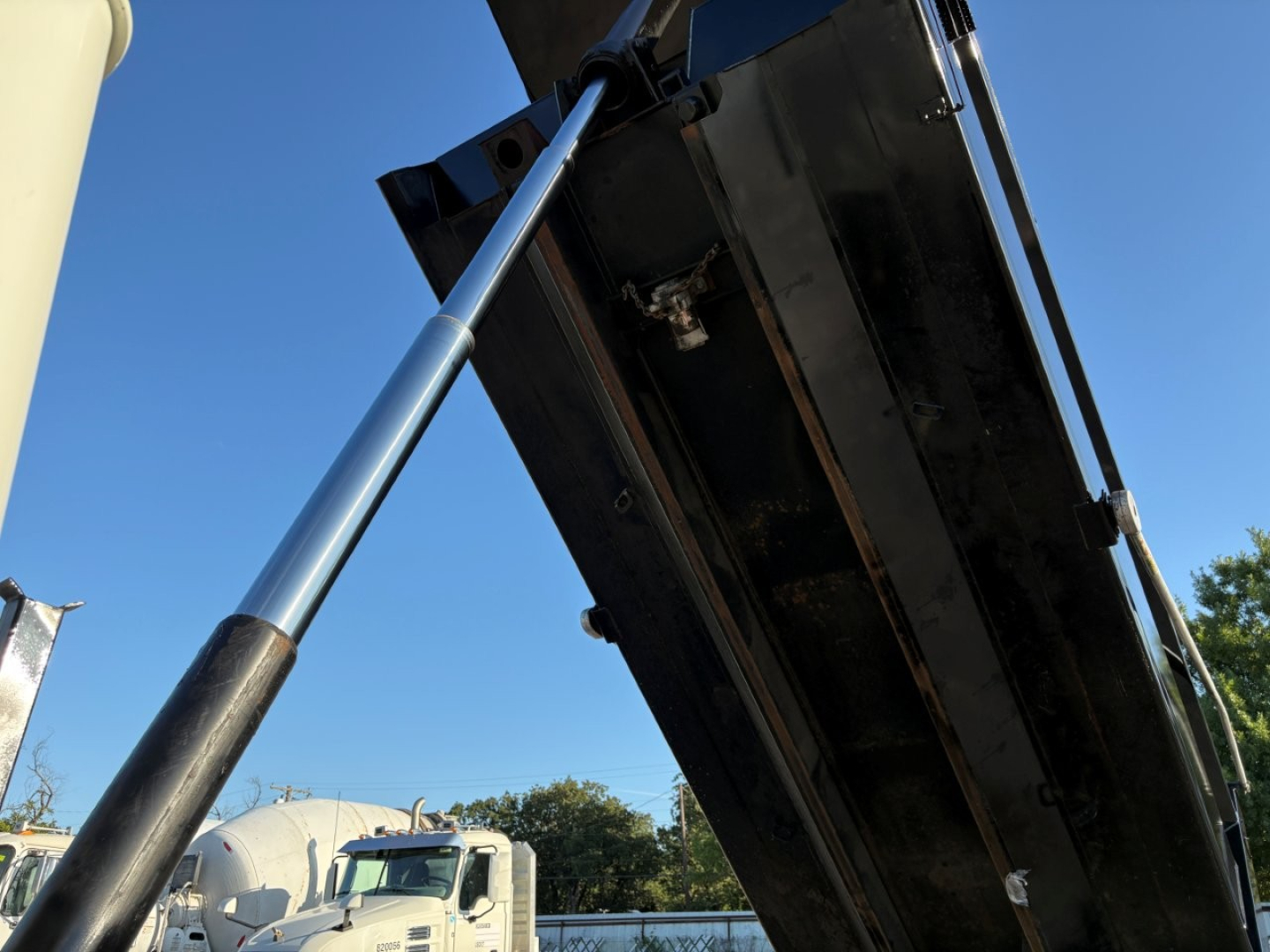 Dump truck bed with hydraulic shocks and underside metal supports visible, Mack GR84F dump truck under raised bed showing black metal surface and hydraulic cylinder.