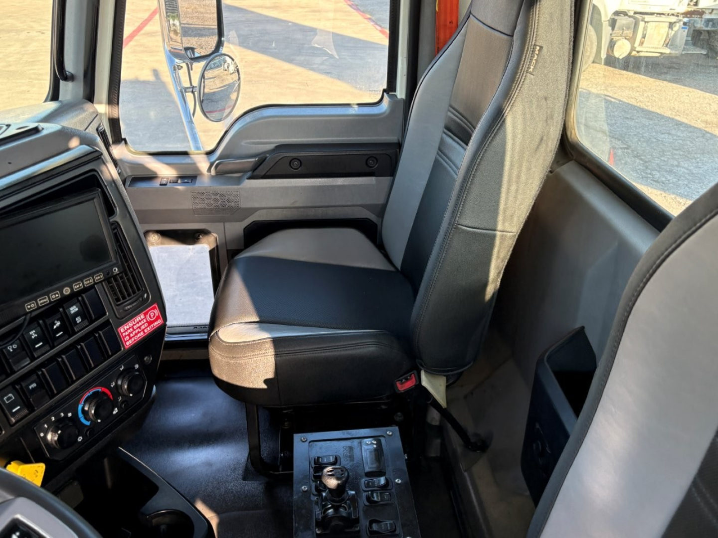 Cab interior of a 2023 Mack GR84F dump truck with grey and black seats, dashboard controls, steering wheel visible, and driver seat area.